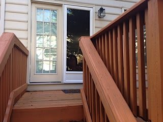 A view of a porch with wooden stairs and a glass door leading into the house.