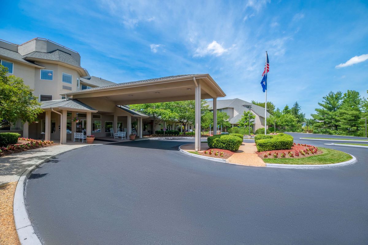 A building entrance with a covered driveway and landscaped surroundings under a clear blue sky.