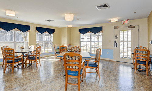A bright dining area with wooden chairs and tables, featuring large windows that allow ample natural light.