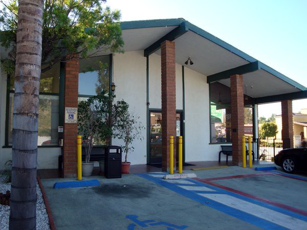 A small drive-thru building with a parking lot and trees around it.
