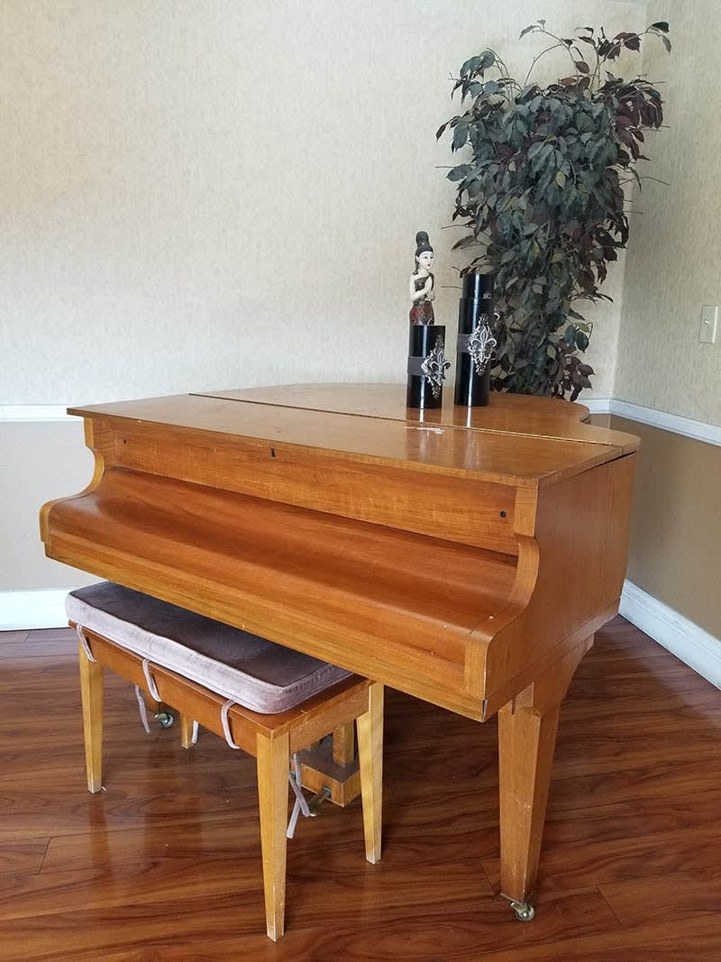 A wooden grand piano with a matching bench, placed indoors with decorative items on top.