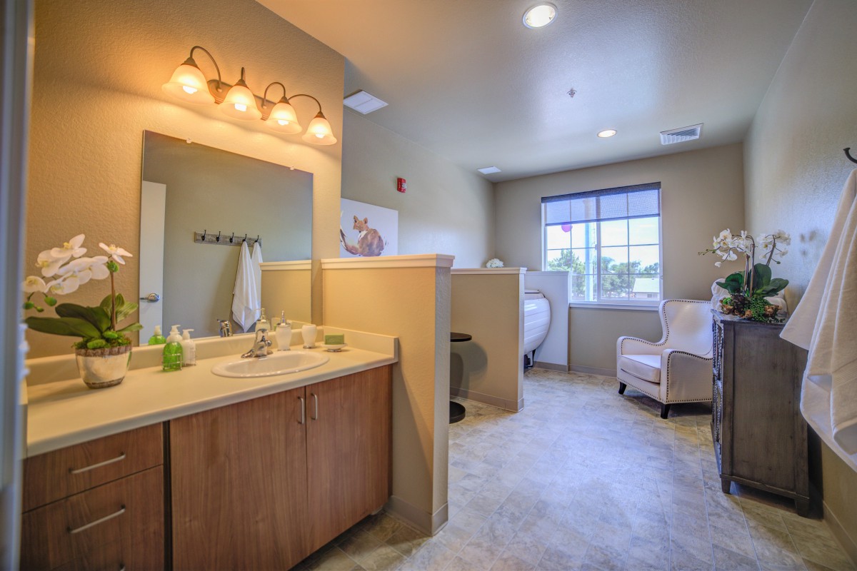 A spacious bathroom with a sink, mirror, and comfortable seating by the window.