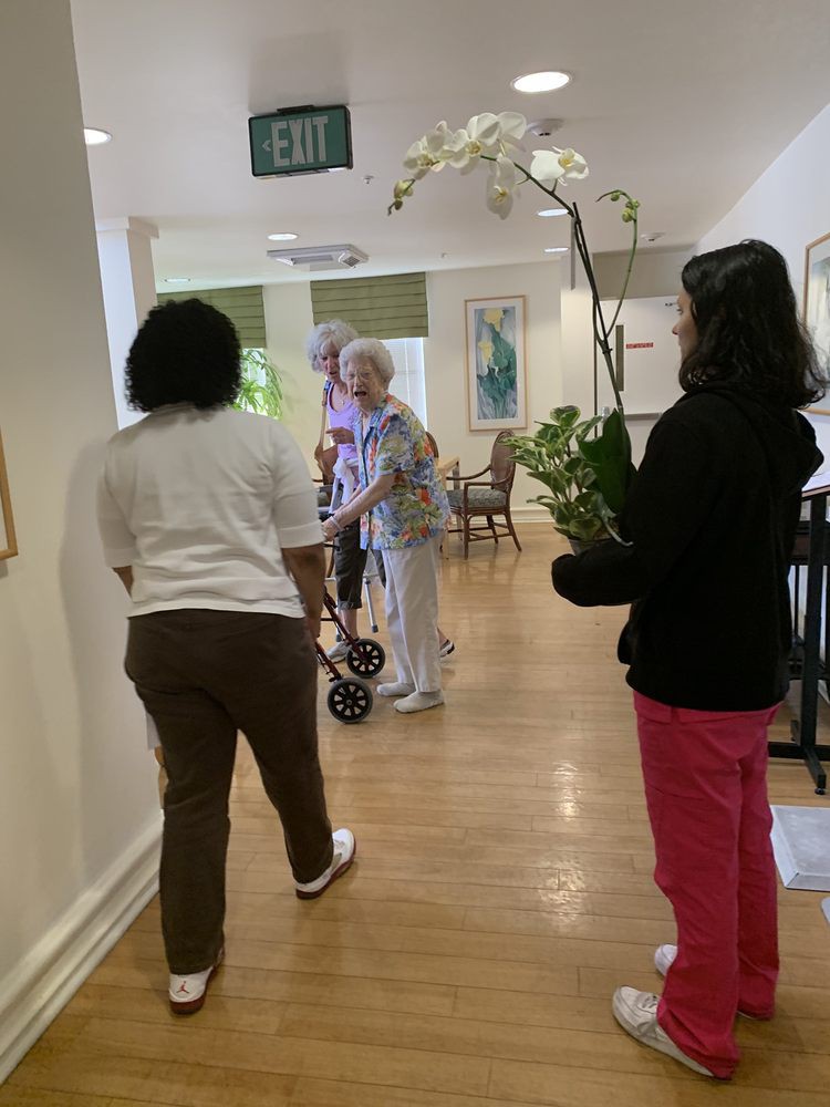 People walking in a nursing home hallway, one person carrying an orchid plant.