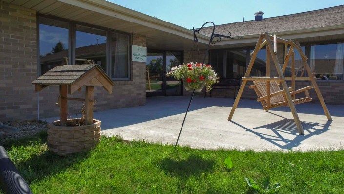 A sunny backyard with a patio, swing, and hanging flowers.