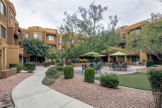 A beautifully landscaped courtyard in an apartment complex featuring outdoor seating and umbrellas.