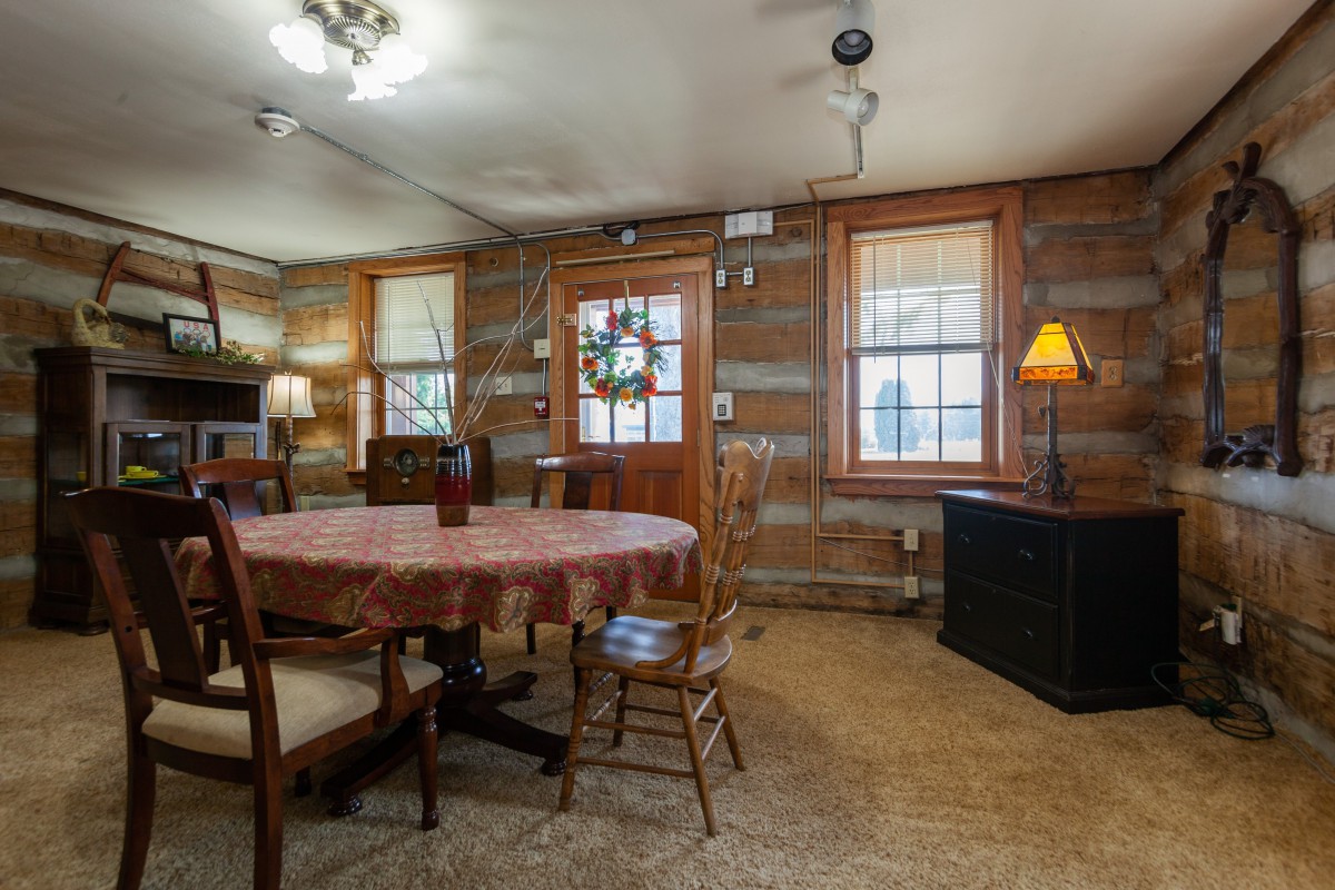 A cozy rustic dining room with wooden log cabin interior featuring a table, chairs, and warm lighting.