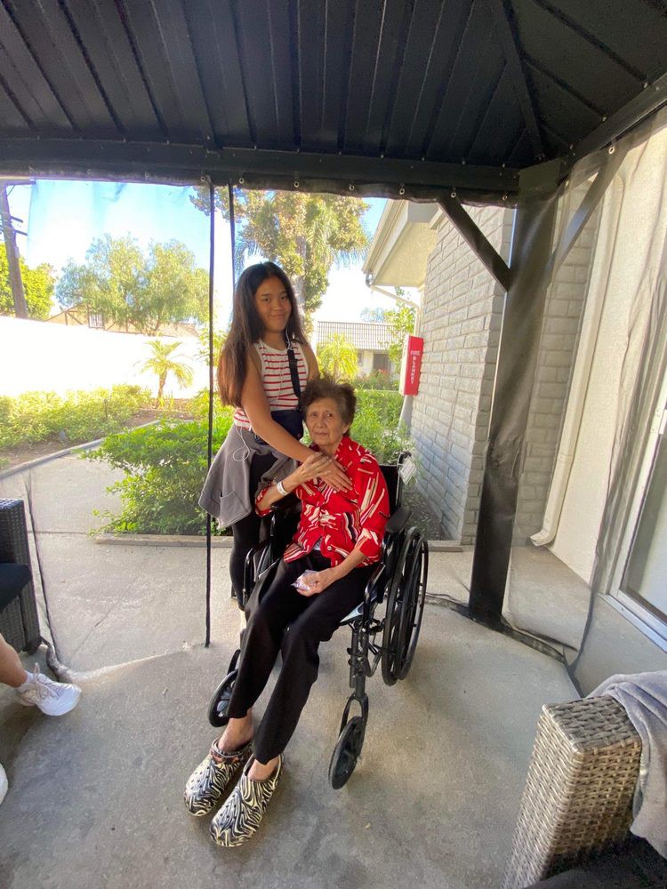 A person in a wheelchair is accompanied by another standing beside them, enjoying time together outdoors.