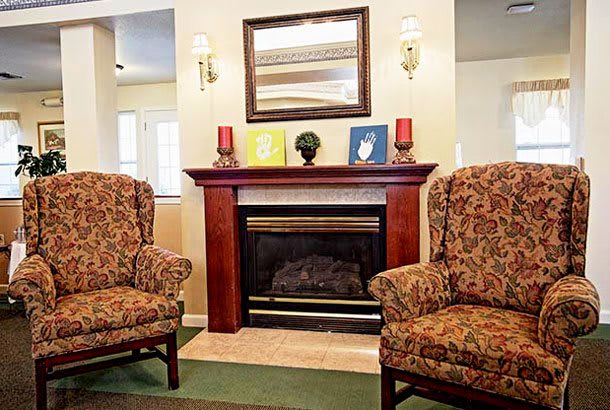 A cozy living room featuring a fireplace, two patterned armchairs, and decorative elements on the mantelpiece.