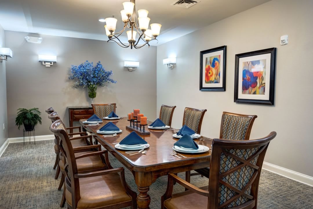 An elegant dining room with a wooden table set for a meal, surrounded by stylish chairs and decorated with artwork and a chandelier.