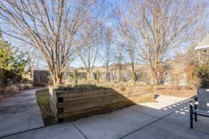 A backyard with a garden area and trees under a clear blue sky.
