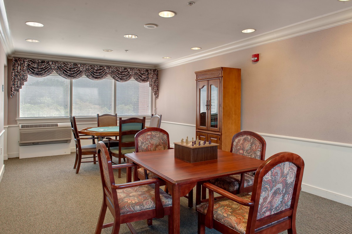 A well-lit dining area with wooden tables and chairs, featuring large windows and decorative curtains.