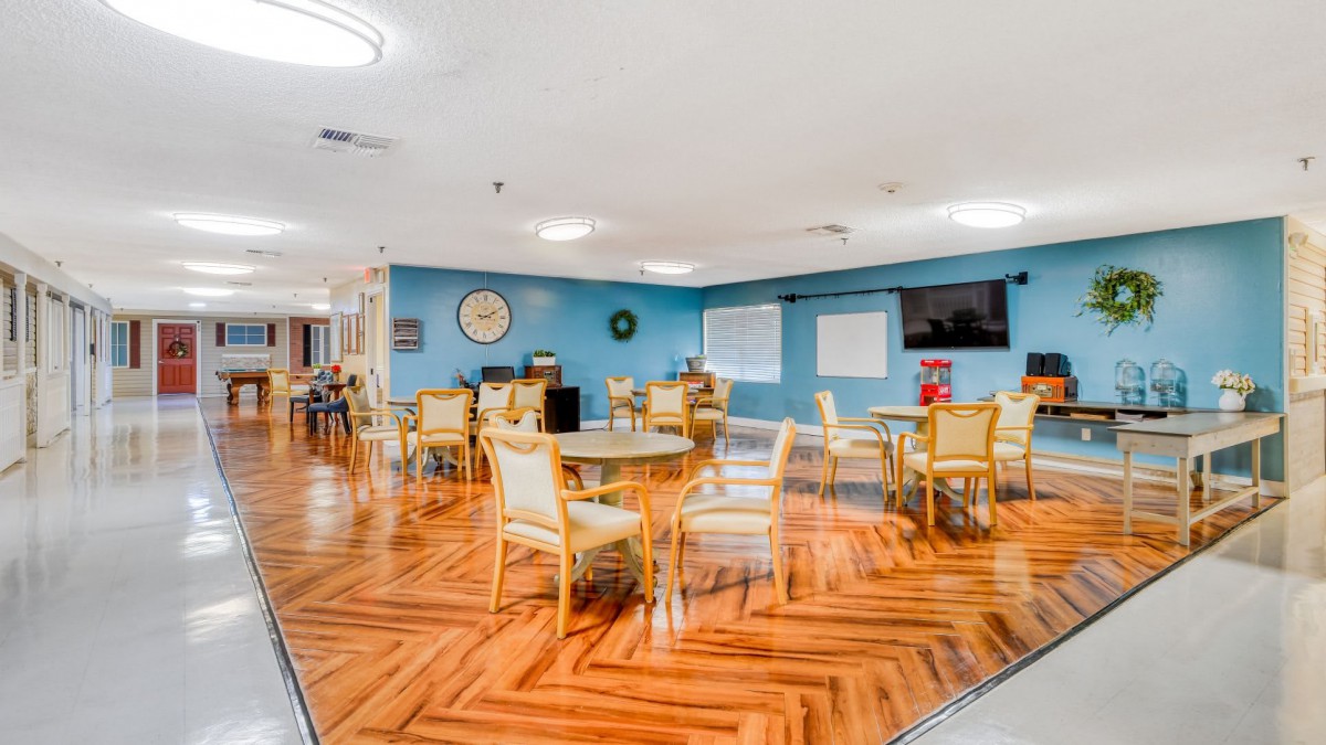 A spacious dining area with wooden flooring, blue walls, and multiple tables and chairs arranged for seating.