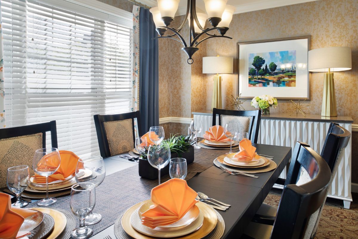 A neatly set dining room table with orange napkins and elegant decor.