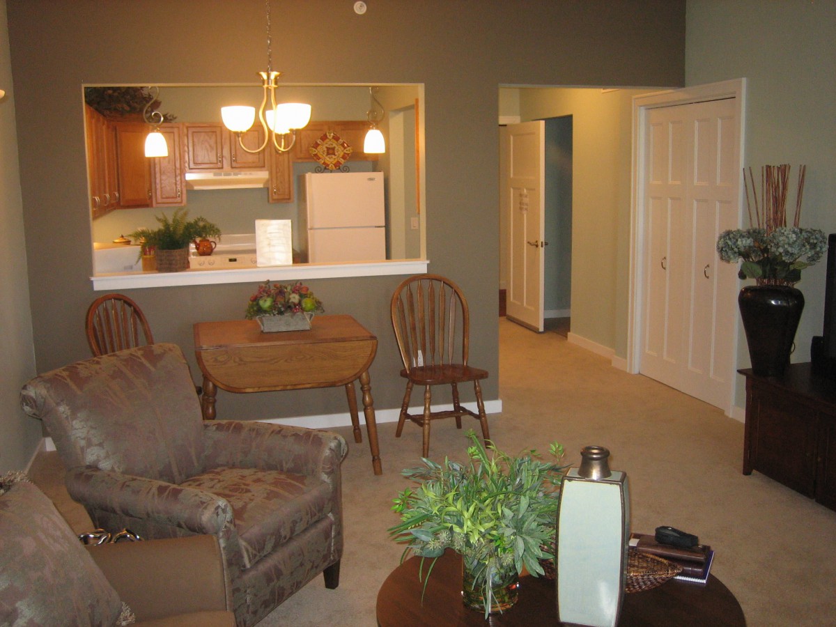 A cozy living room with an open view into the kitchen, featuring comfortable seating and warm lighting.