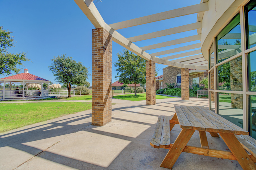 A serene outdoor patio area with a wooden table, surrounded by greenery and sunlight.