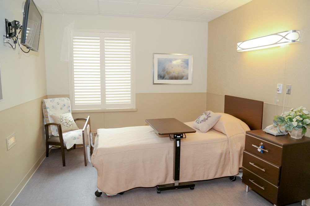 A clean and tidy hospital room with a bed, overbed table, and a window with blinds.