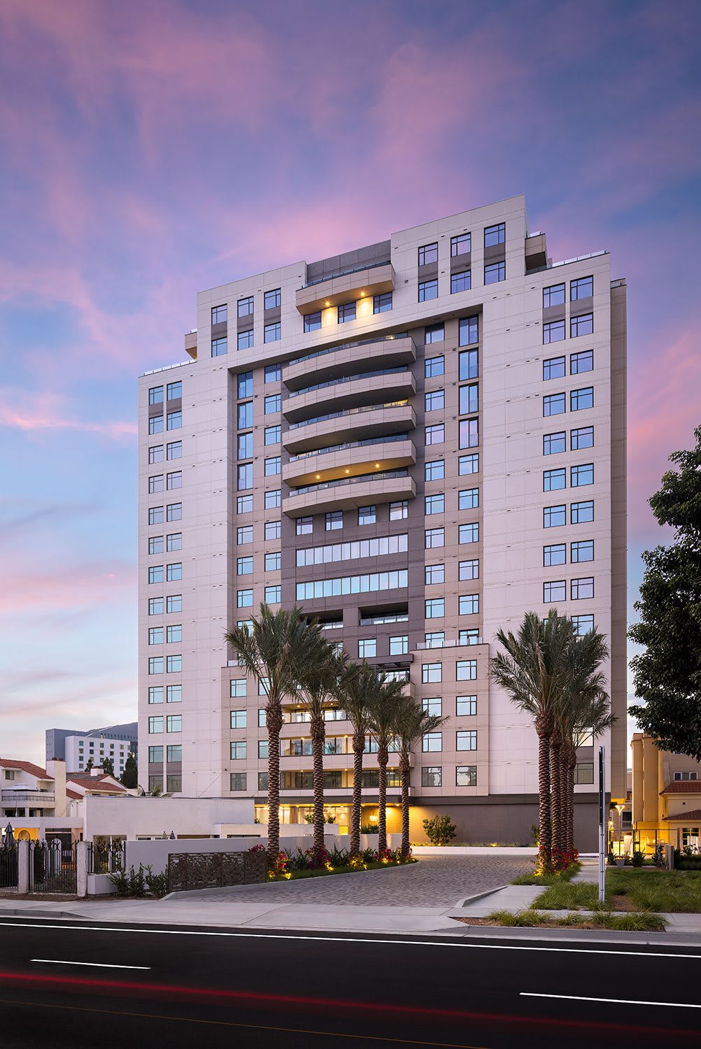 A modern hotel building at sunset with palm trees in the foreground.