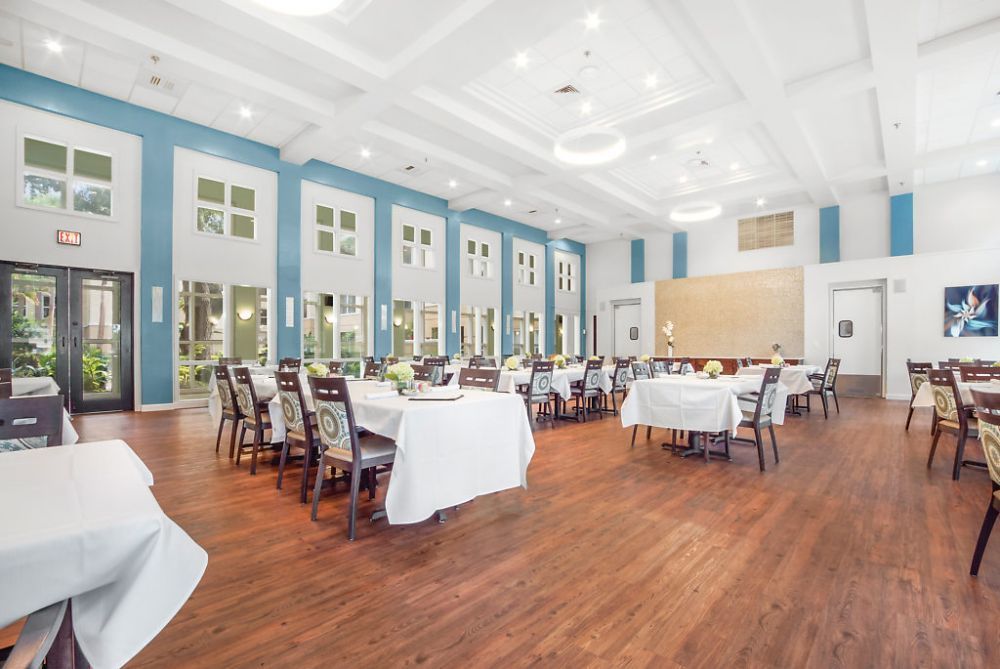 A spacious and elegantly decorated dining room set up with tables and chairs, featuring large windows and bright lighting.