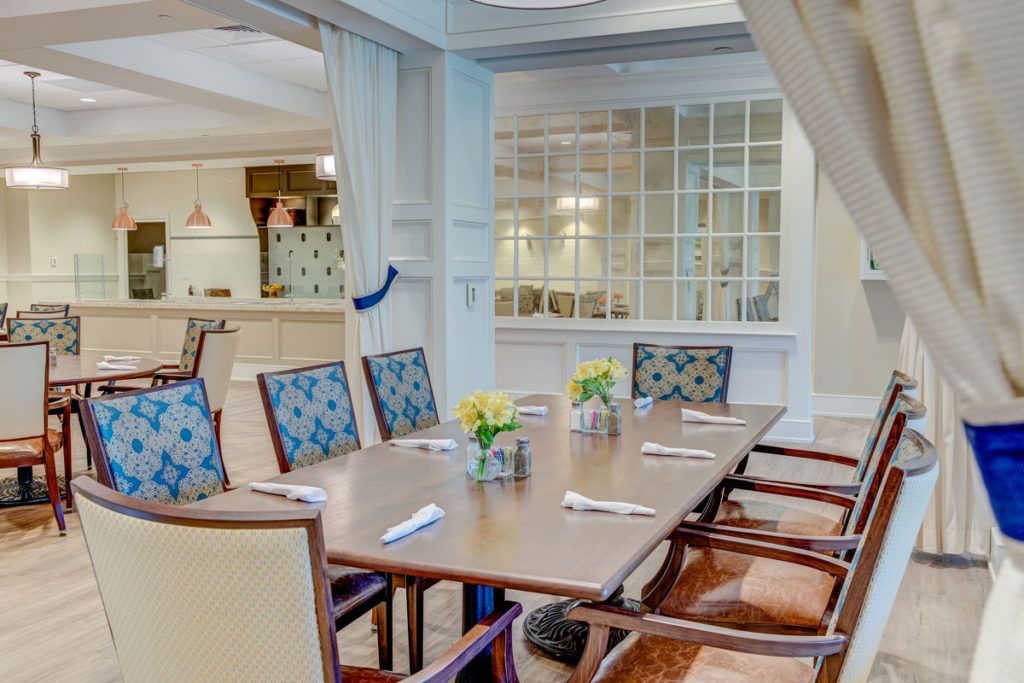 A neatly arranged dining room featuring a wooden table with chairs, adorned with vases of yellow flowers and set with cutlery.