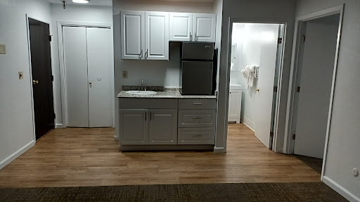 A modern kitchen featuring white cabinets and a stainless steel refrigerator, with wooden flooring.