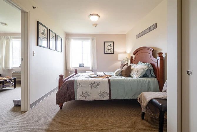 A cozy bedroom with a neatly made bed, decorative pillows, wall art, and a window letting in natural light.