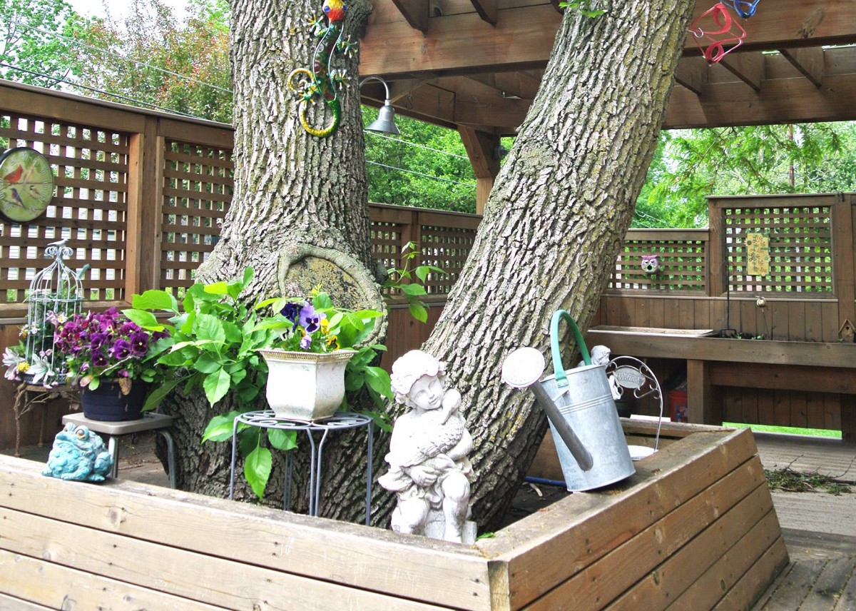 A charming garden setup featuring a tree surrounded by plants and decorative items, including a sculpture and a watering can.