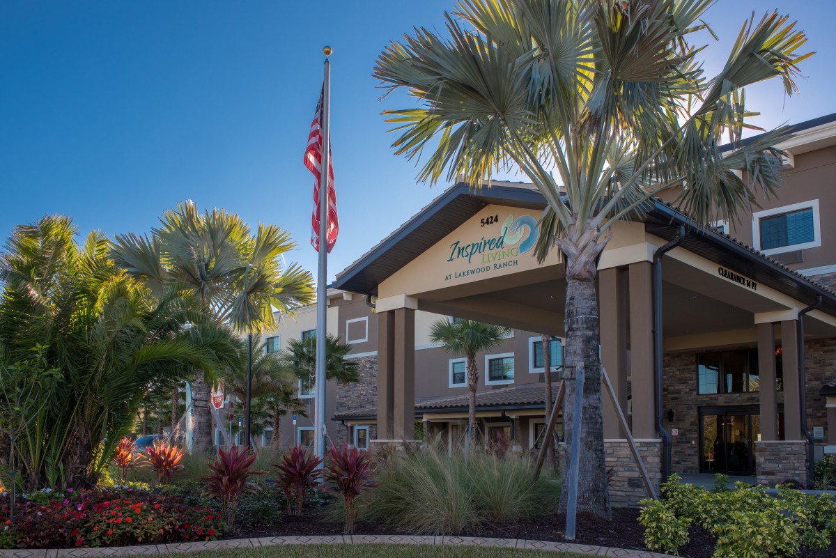 A welcoming building entrance surrounded by palm trees and well-maintained landscaping, with a flagpole displaying a flag.