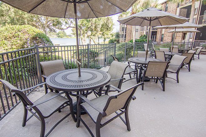 An outdoor patio area with tables and chairs under large umbrellas, enclosed by a fence.