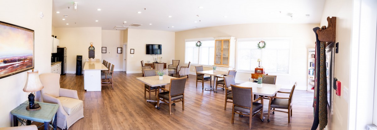 A bright dining area with several tables, chairs, a television, and wooden flooring.