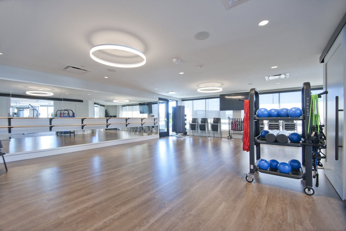 A spacious and modern exercise room with mirrors, fitness equipment, and wood flooring.
