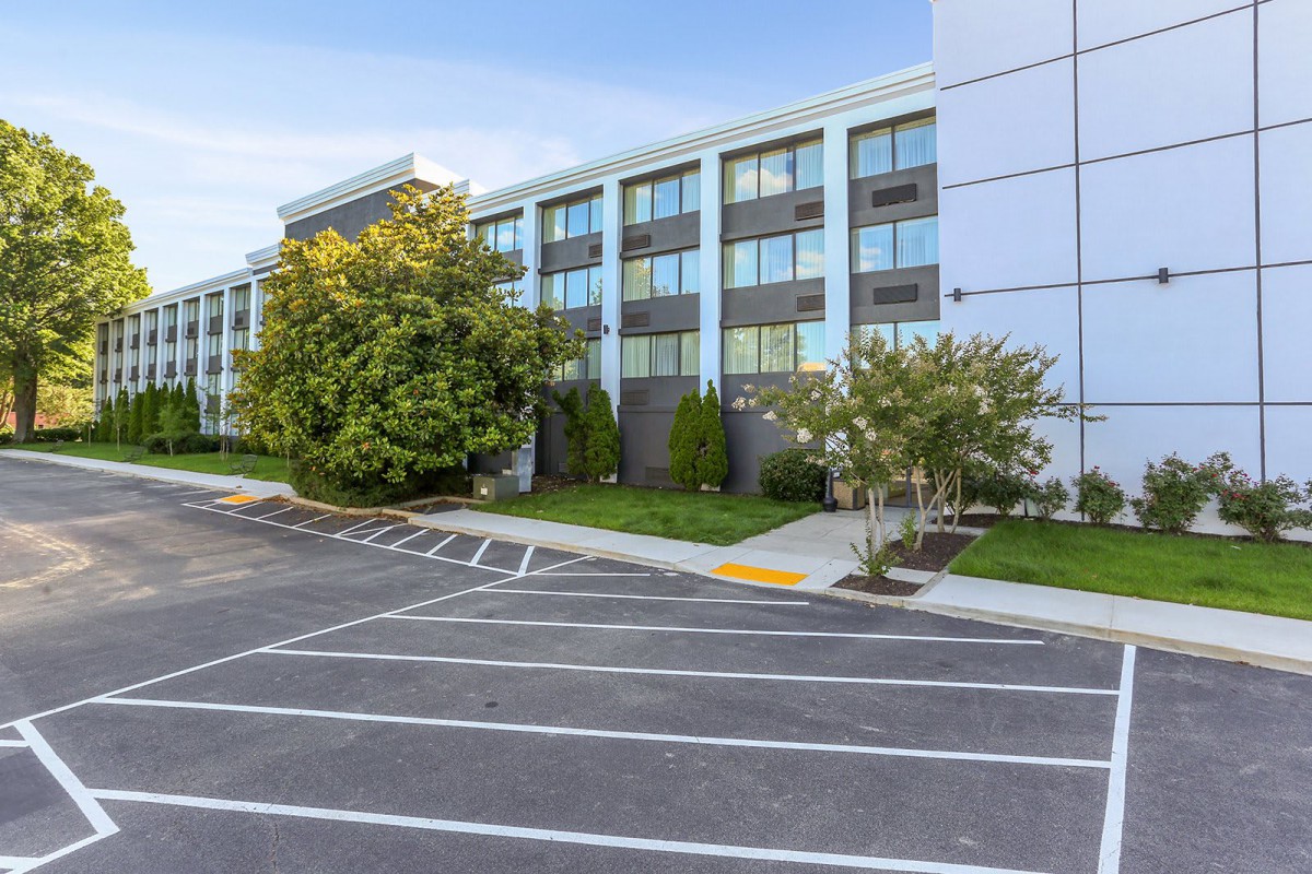 A modern building with large windows and a parking lot, surrounded by greenery.