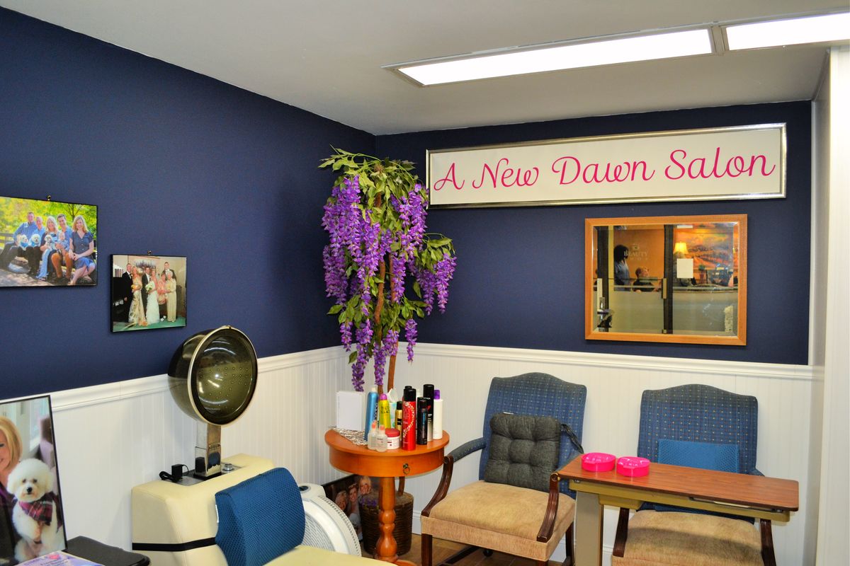 A cozy salon waiting area with chairs, a hair dryer, and decorative plants.