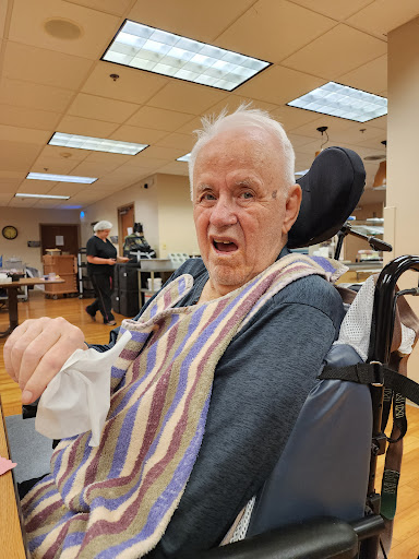 An elderly man enjoying a moment in a care facility, smiling while seated in a wheelchair.