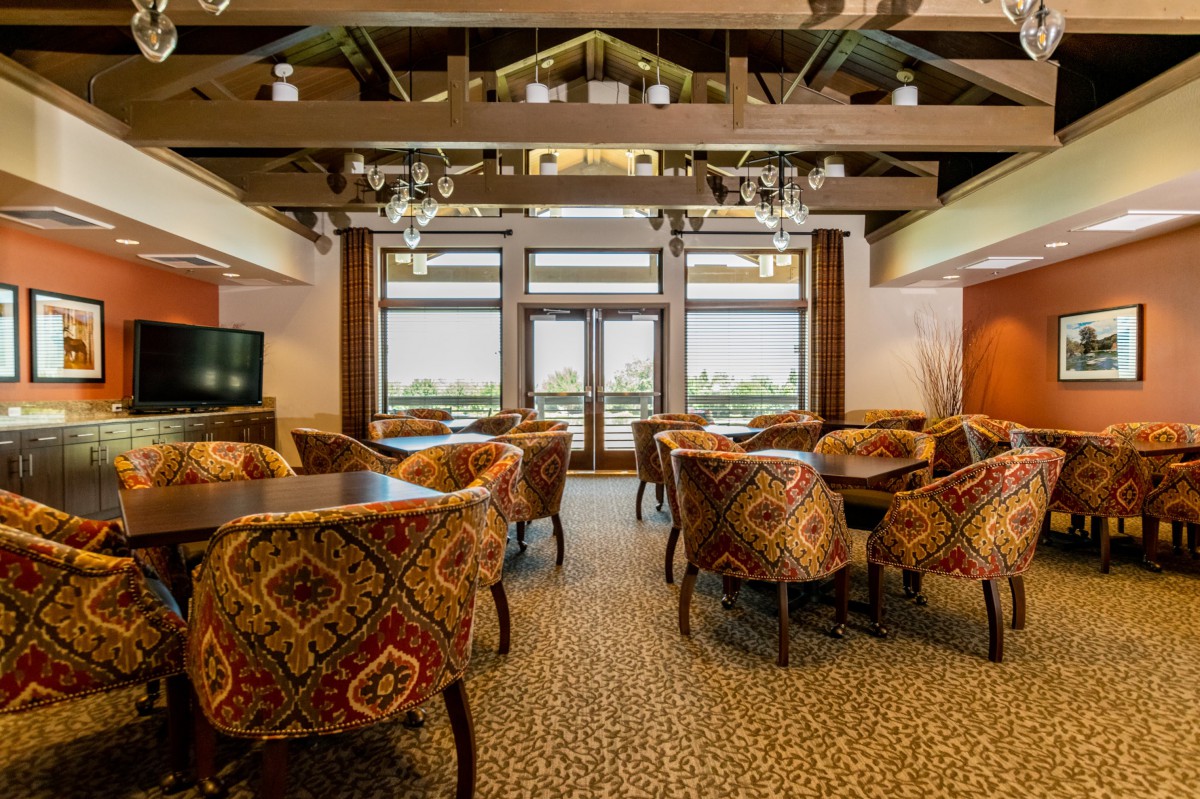 A cozy restaurant dining room with patterned chairs and tables, featuring large windows and a warm atmosphere.