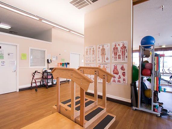 A physical therapy room featuring exercise equipment, anatomical posters, and fitness balls for rehabilitation exercises.
