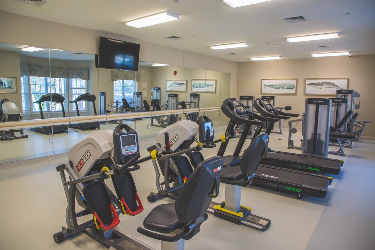 A modern gym with various exercise machines, including treadmills and stationary bikes, in a well-lit indoor space.