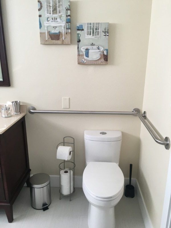 A bathroom with a toilet, safety grab bars, and various accessories.