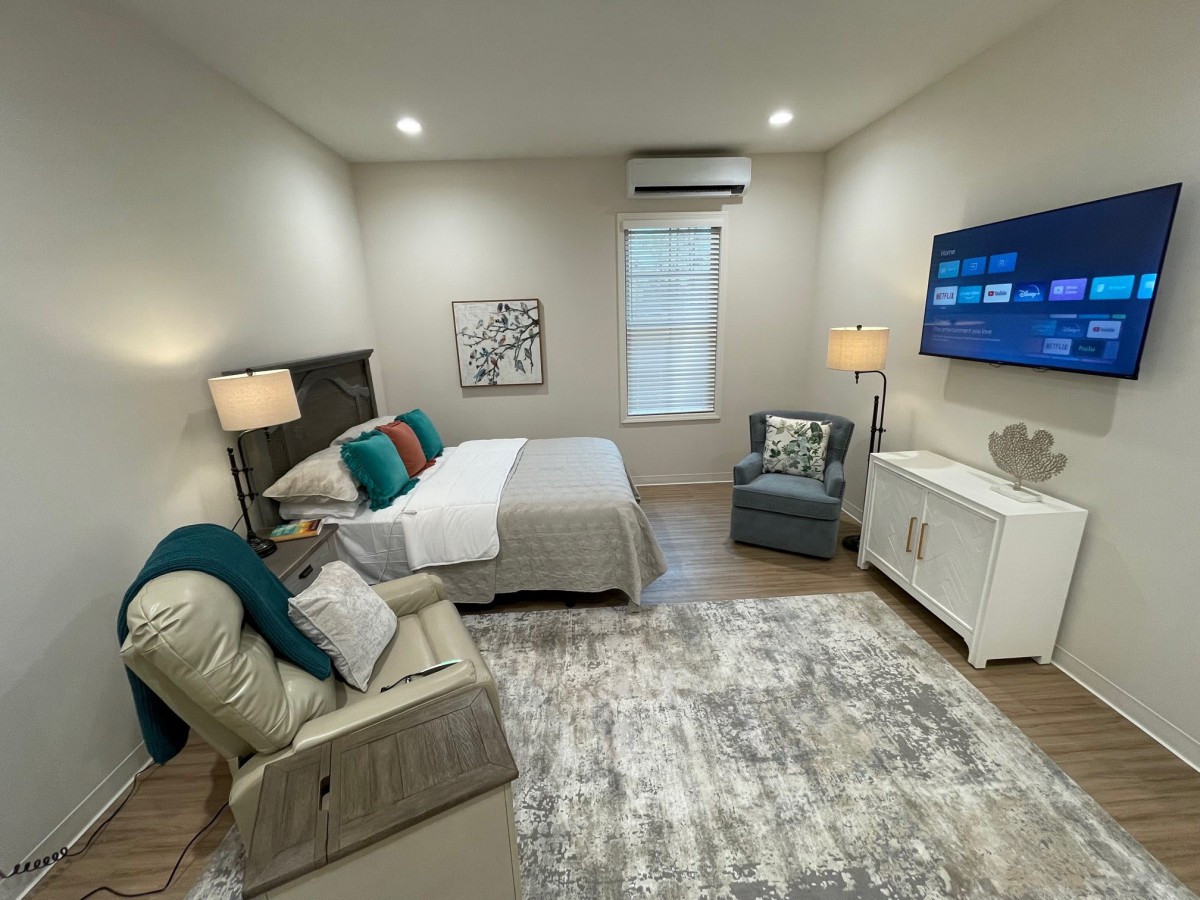 A modern and cozy bedroom with stylish decor, featuring a bed, armchair, lamps, and a wall-mounted television.