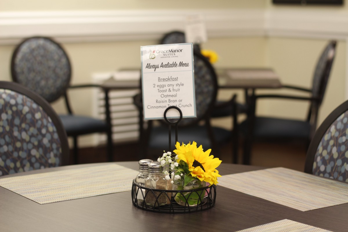 A dining table with a centerpiece featuring a sunflower and a menu stand.
