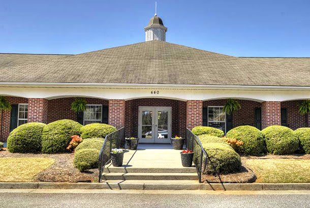 A brick building with a central entrance surrounded by landscaped shrubs.