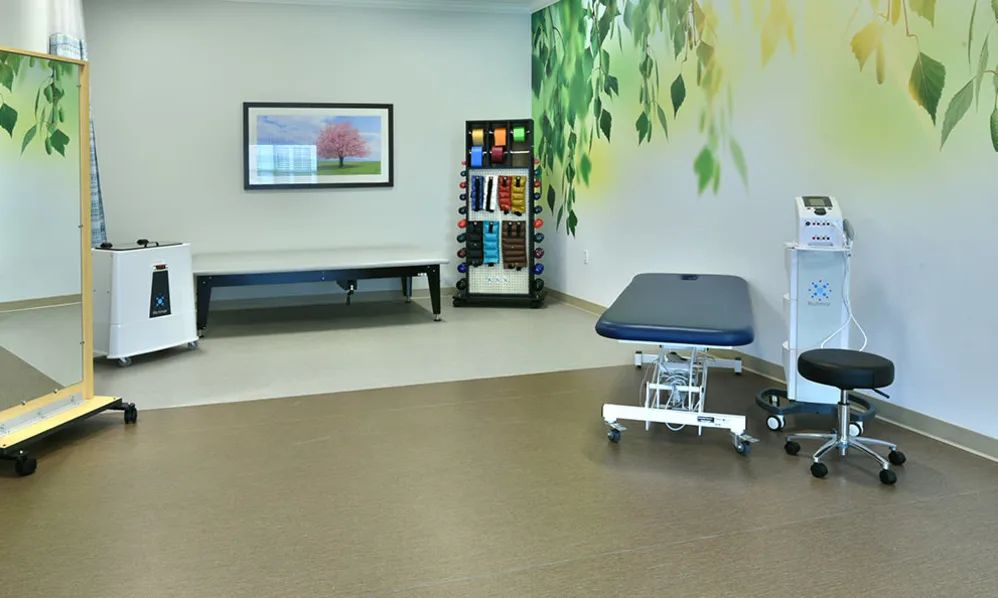 A well-lit clinic room featuring an examination table, a waiting area with benches, and decorative wall art.