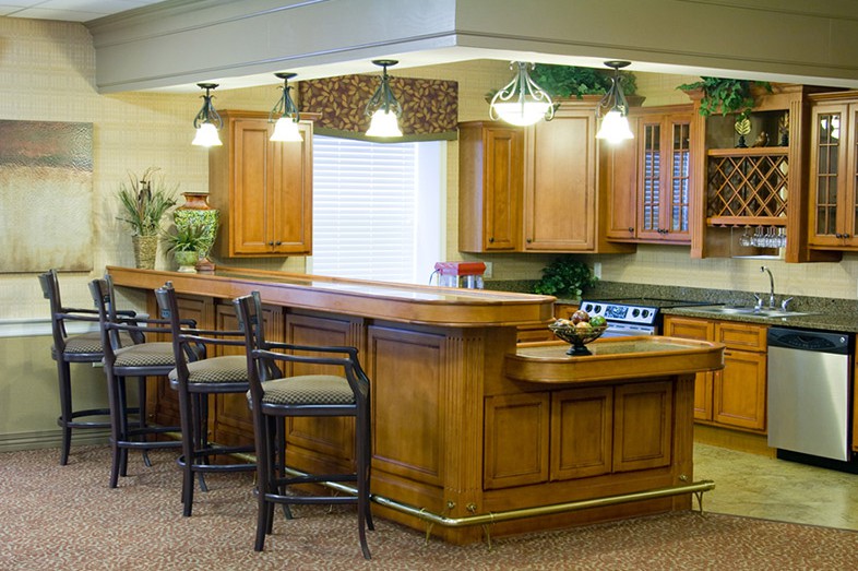 A modern kitchen with wooden cabinets, a large central countertop, bar stools, and stylish lighting.