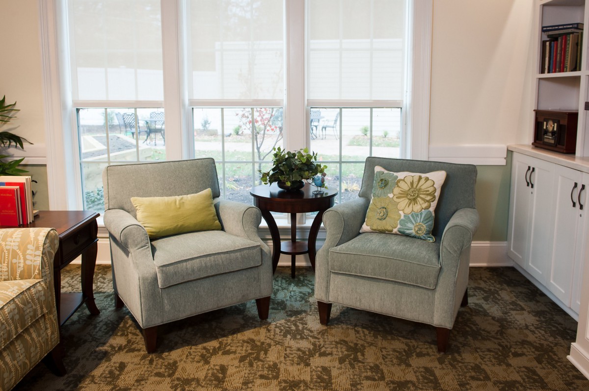 Two armchairs with cushions arranged by a window and a small side table with a plant.