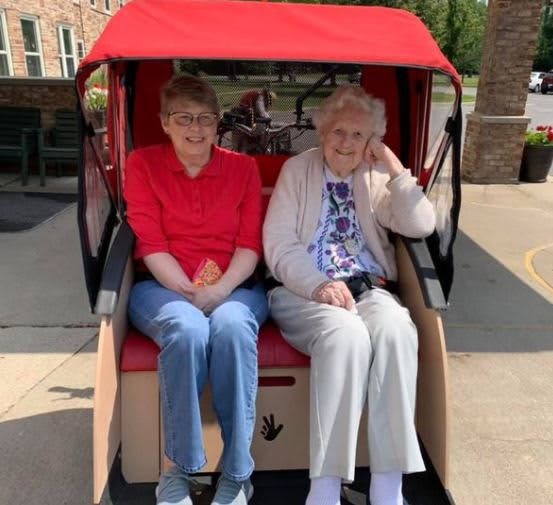 Two elderly women sitting in a rickshaw with a red canopy.