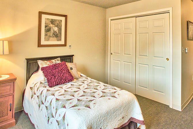 A cozy bedroom with a single bed and decorative pillows, featuring wall art and closet doors.