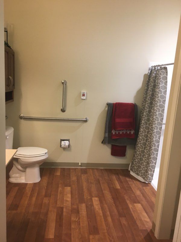 An accessible bathroom with a toilet, handrails, towels, and a shower curtain on a wooden floor.