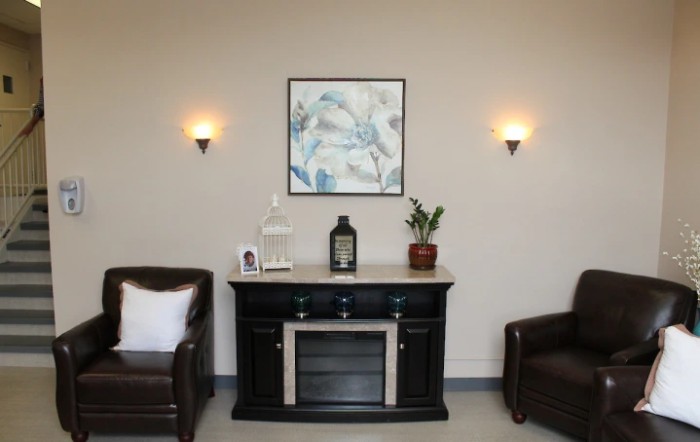 A stylish living room interior featuring a dark cabinet with decor, flanked by two leather chairs and illuminated by wall sconces.