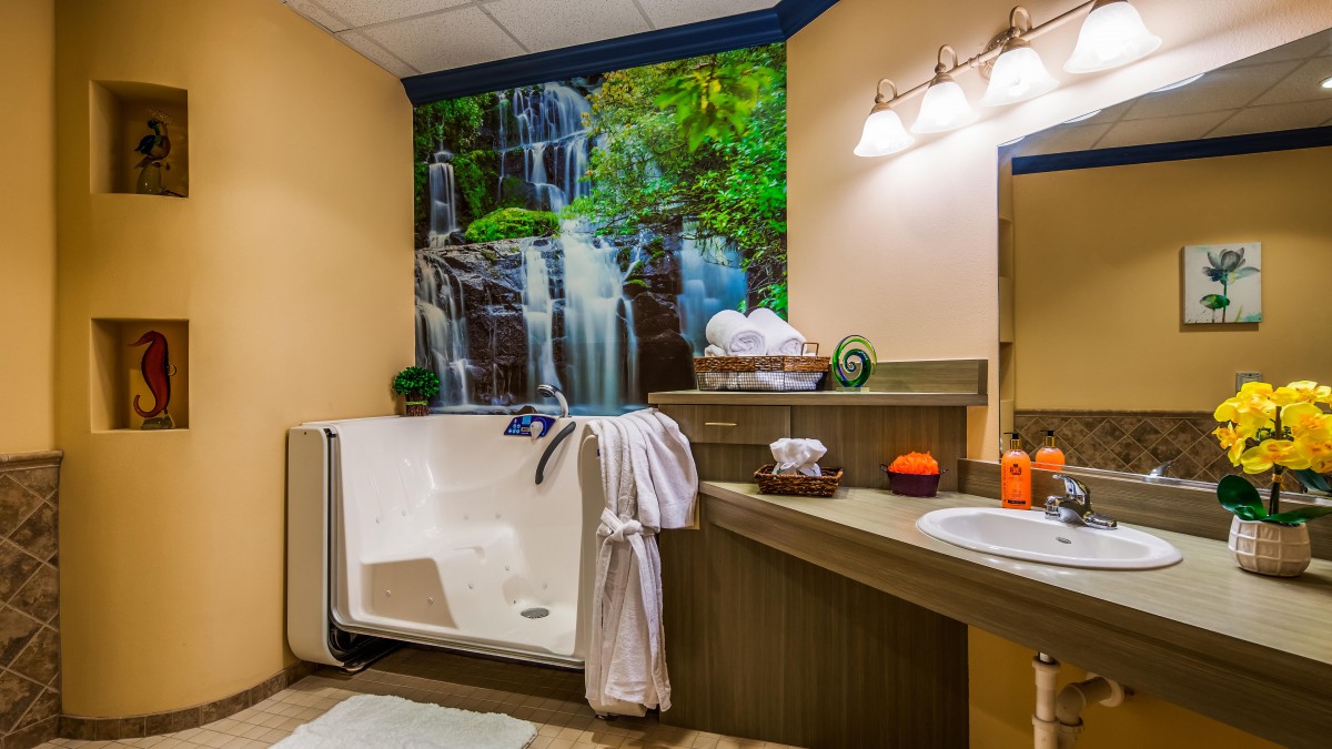 A cozy bathroom featuring a walk-in tub with a scenic waterfall mural, complete with a robe and towels for comfort.