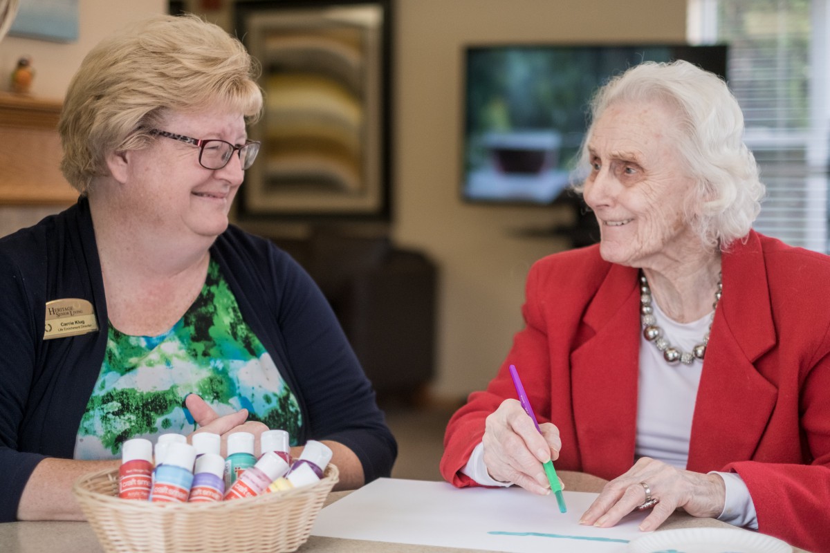 Two elderly women engaging in a conversation with art supplies on the table.