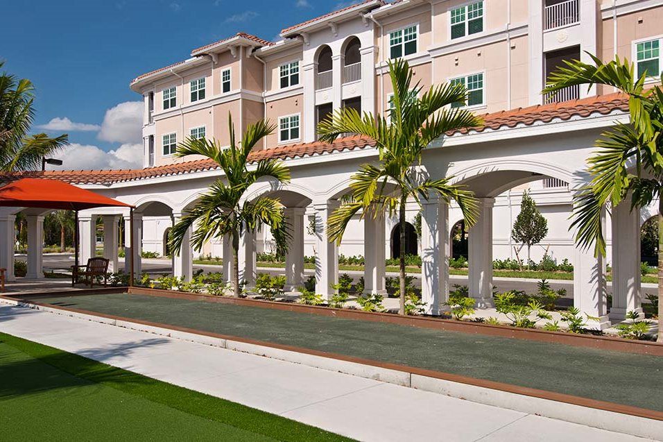 A sunny view of a multi-story building with palm trees lining a walkway.